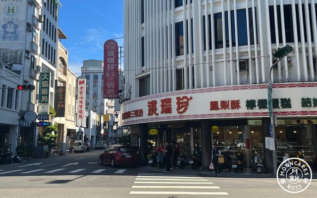 A round building with thin white columns, with a large shopfront signfor 洪瑞珍 advertising sandwiches, pineapple cakes, and more