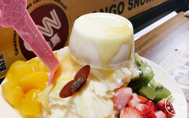 A large bowl of shave ice with fresh mango, strawberry, kiwi, and an entire flan